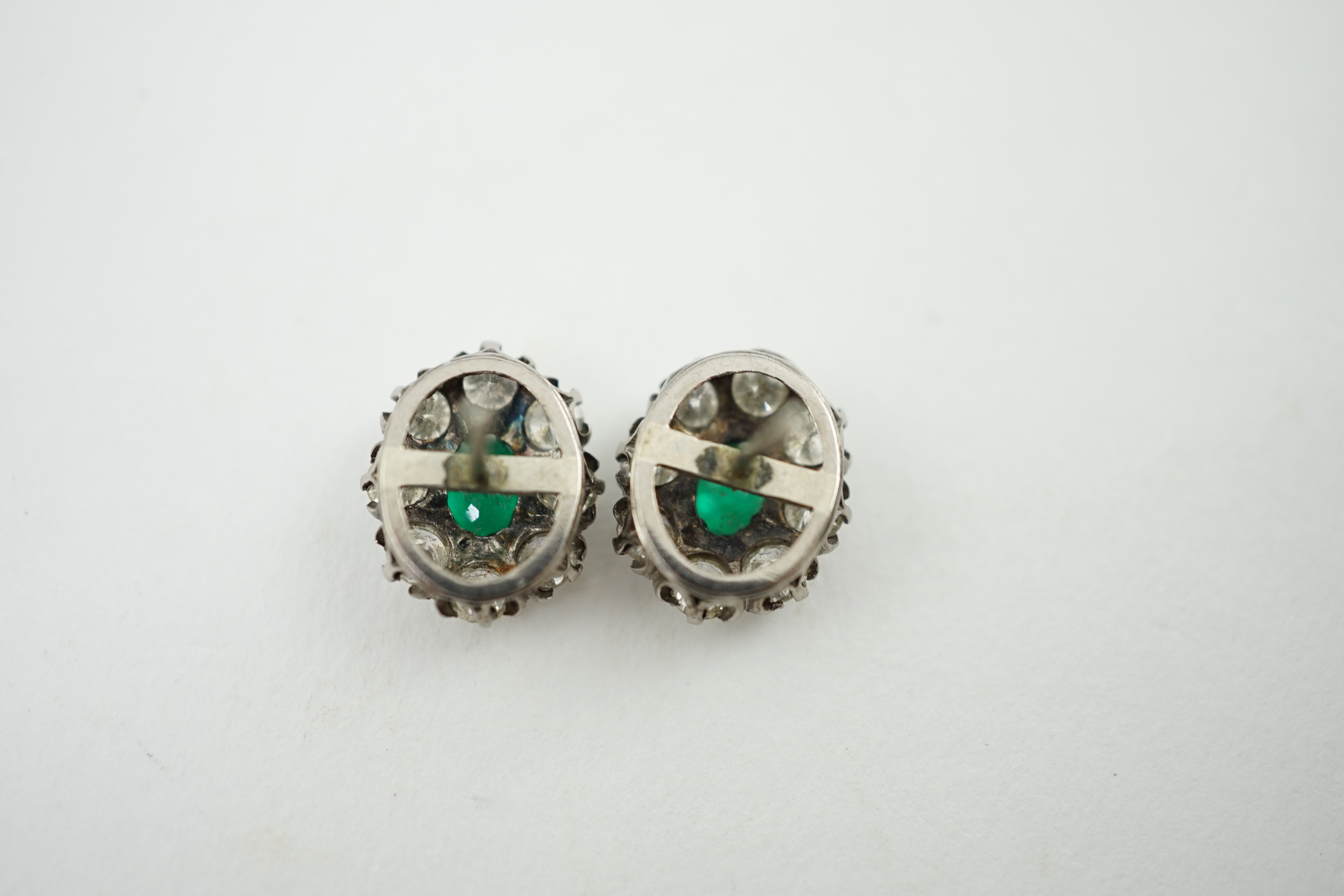 A pair of white gold, single stone emerald and eight stone diamond set oval cluster earrings